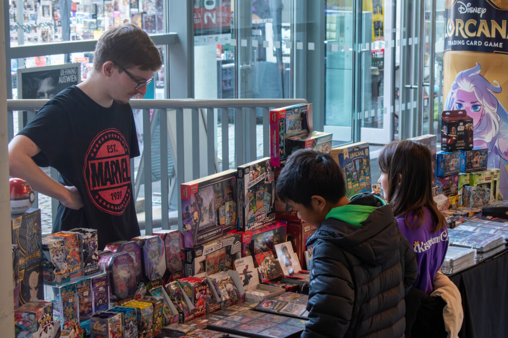 Junge schaut sich auf dem Stand um. Verkäufer steht daneben. KingdomCon 2025